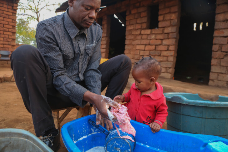 Joseph Bistoni takes care of his 15-month old daughter Desire at their home in Mbirimtengerenji Village, Malawi. Bistoni takes care of Desire while her mother looks after her morning chores. In Malawi men traditionally don't get involved in child rearing but Bistoni learned about the importance of male involvement through the Conrad N. Hilton funded CRS project called THRIVE II. This project seeks to give children the best possible start in life. Focusing on the first 1,000 days from when a child is conceived through the first two years of life, THRIVE II empowers parents with knowledge about early childhood development and how to stimulate thought and independence in young children. Participants learn the importance of bonding while still in the womb and the critical role father's play in child care. Lessons on toy making, positive discipline, and nutrition are at the core of THRIVE II.