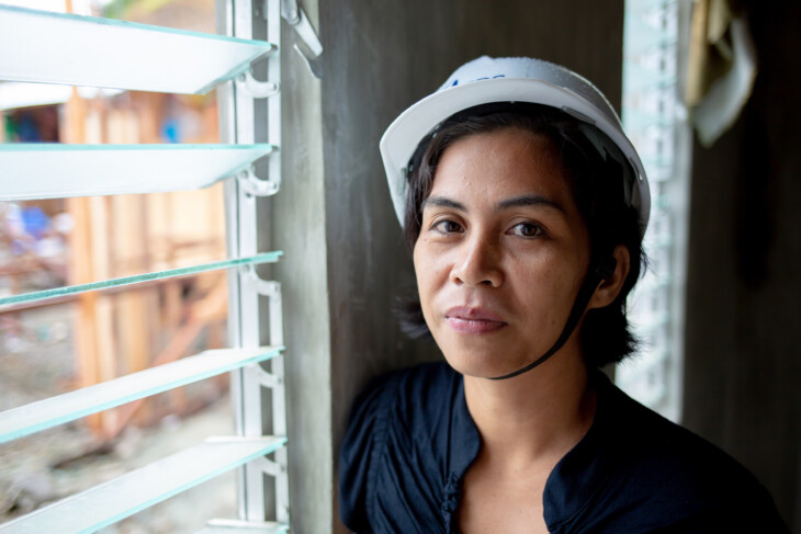 Girlita “Girli” Ascalona, 37, will own one of seven pilot homes in the Anibong resettlement community. She is about to be evicted from her current home, one that floods in heavy rain and sits dangerously close to a main road with fast-moving traffic. She is most excited to have title to her land, something that felt out-of-reach on her own even though her husband has a steady job in sales. CRS is helping her to navigate the complicated, paper-based process of purchasing her small lot, which measures just 4x6 meters. She said that this land, which will belong to her free and clear in 10 years, will be her inheritance for her children, a place they can always come home. The house includes typhoon and earthquake-resilient construction, rainwater catchment system, indoor toilet, full electrical wiring, and is designed to safely hold a second story if Girlita decides to add another level in the future. This will be the first time Girlita lives in a home with running water. In these images, Girlita sees her complete new home for the first time, turns on her running water, and is also photographed outside with an embankment wall in the background, part of the core community infrastructure. Project background: Super Typhoon Haiyan, known locally as Yolanda, wreaked catastrophic devastation across the Philippine islands of Leyte and Samar on November 8, 2013, claiming more than 6,300 lives and leaving infrastructure and neighborhoods in ruins. At least 1.1 million homes were damaged or destroyed. Among the most devastated areas was the coastal district of Anibong in Tacloban, on Leyte island, where the super typhoon washed away or destroyed the vast majority of houses and local infrastructure. The damage was so severe, and the risk of further destruction in future storms so severe, that the Government of the Philippines declared it a “no-dwell zone” and compelled residents who had lived in the coastal area for generations to relocate elsewhere. Nearly five years