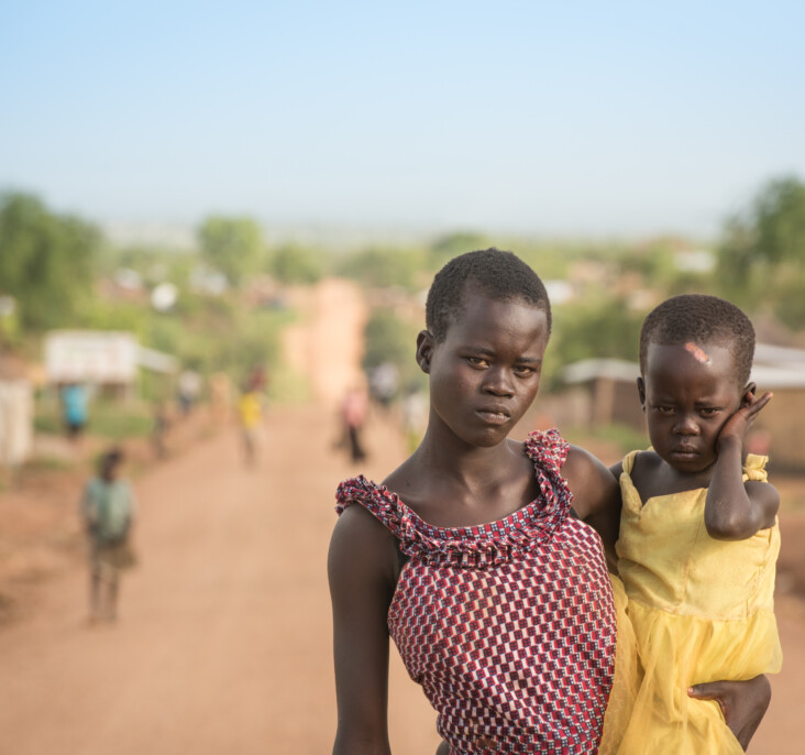 Annet holds her little sister, Gladys. They faced danger from rebels on the long road from South Sudan to Bidi Bidi. “They wanted me to untie Gladys from my back and leave her there,” Annet remembers. “I refused. I said, ‘If it means dying, we shall all die here.’ They beat me but they let us go.” Photo by Philip Laubner/CRS.