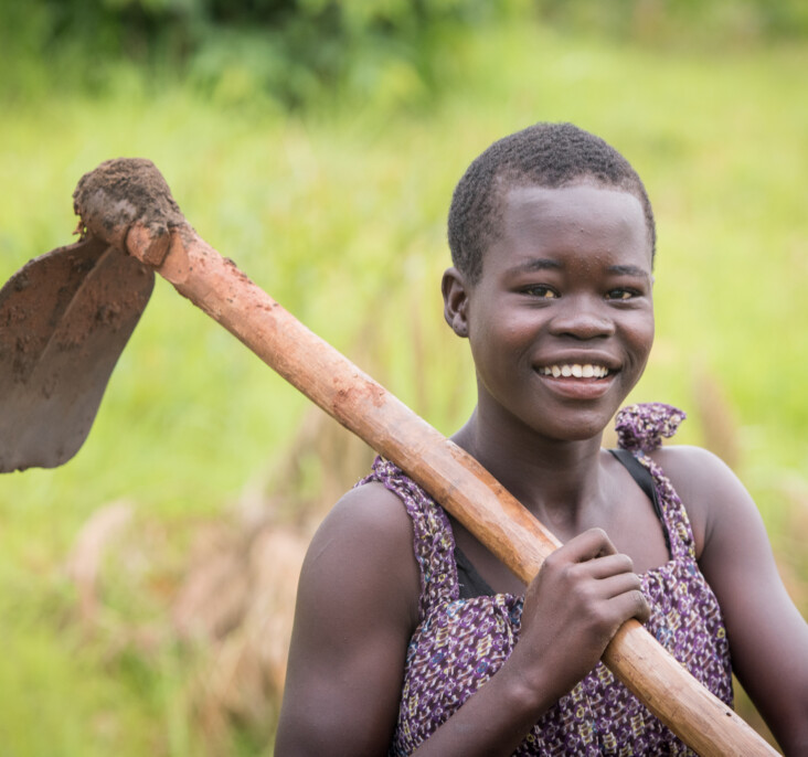 Annet Konga uses a tool to collect mud near her future home. It will be used to coat the outside of the new shelter CRS is building for her family. Photo by Philip Laubner/CRS.