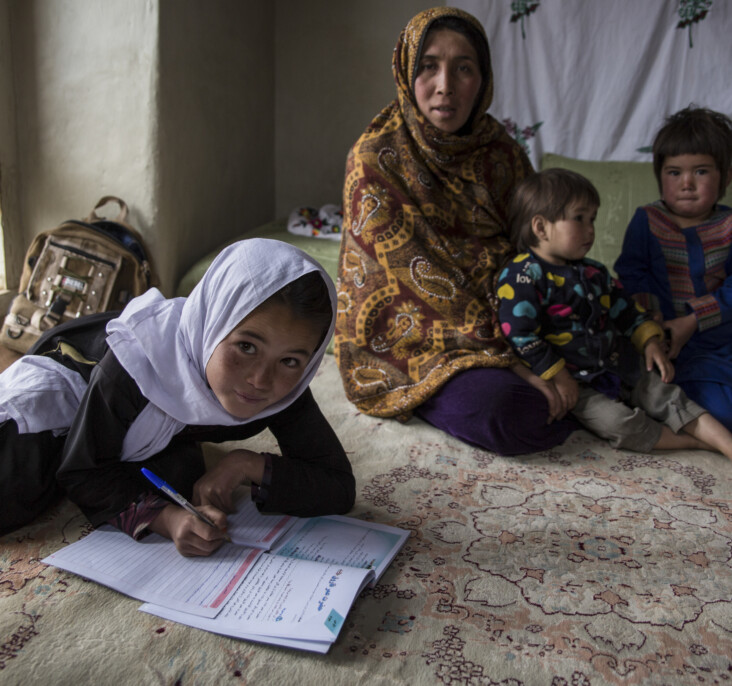 Morzal, 10, does homework surrounded by her family. She is enrolled at a CRS primary school in her remote Afghan village. Morzal wants to study to become a teacher herself one day. Photo by Stefanie Glinski for CRS